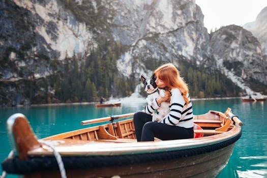 Red-haired woman cuddles dog on a wooden boat at Lake Braies with mountains in the background.