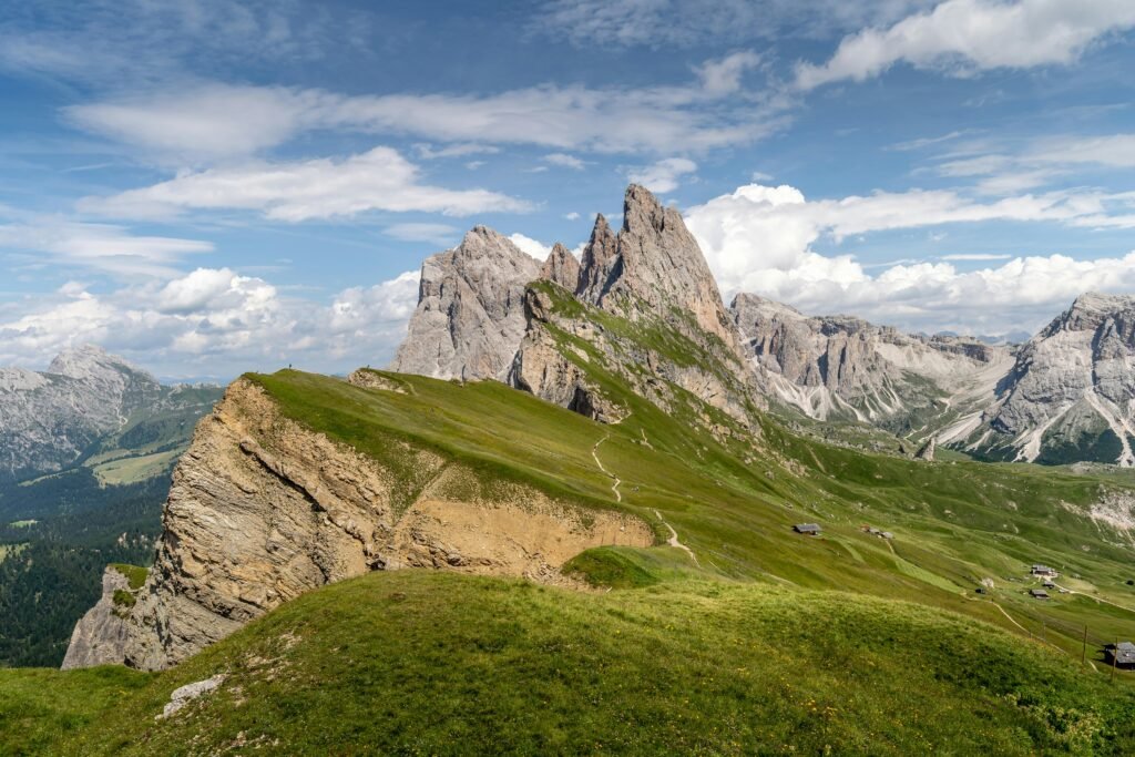 Scenic landscape of the Dolomites with rugged peaks and lush green hills under a blue sky.