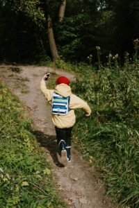 A child in a yellow jacket running down a forest path, holding a smartphone.