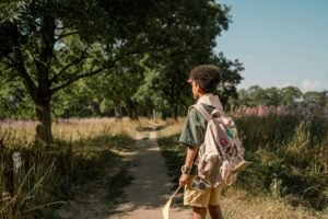 Young boy scout with backpack walking through a forest trail on a sunny day.