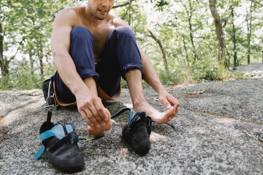 Shirtless man sitting on a rock, resting with climbing shoes nearby.