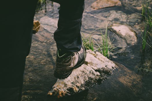 A hiker's boot steps on a rock in a flowing stream, symbolizing outdoor adventure and exploration.