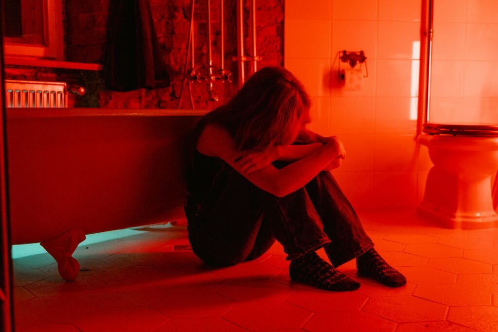A woman sits alone in a red-lit bathroom, conveying emotions of loneliness and introspection.
