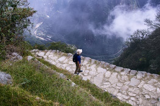 A lone hiker enjoys a breathtaking view from a mountain trail, surrounded by mist and nature.