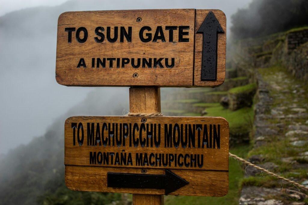 Wooden signpost directing to Sun Gate and Machu Picchu Mountain on misty day.